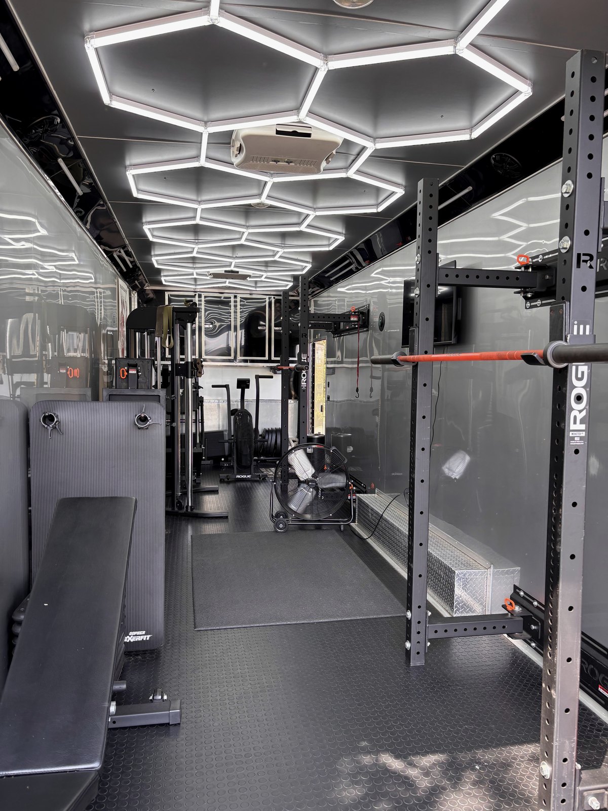 Inside the mobile gym: a rack, bench and training floor under overhead lighting